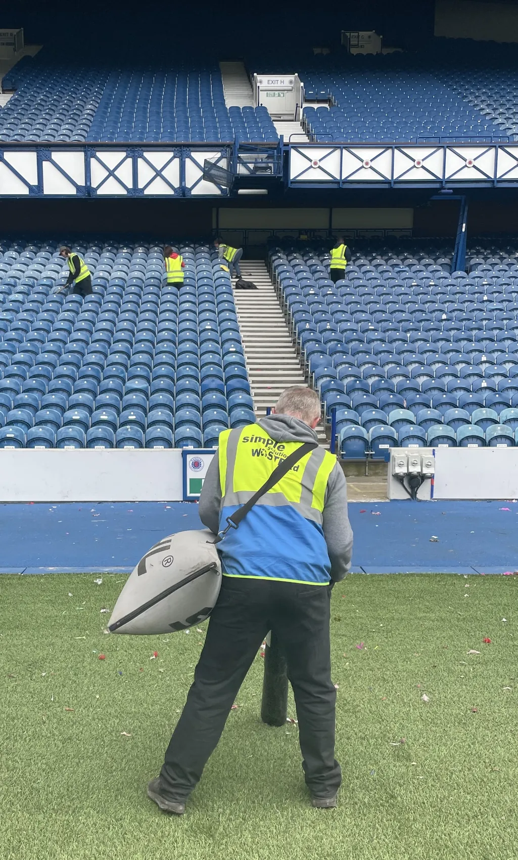 SWS cleaning operative on the pitch with other team members cleaning stadium seating at Ibrox